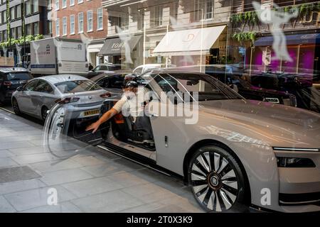 Con i riflessi di altre vetture parcheggiate in strada, un potenziale acquirente raggiunge la porta di una lussuosa Rolls-Royce nello showroom di Mayfair, dove un'auto viene esposta, il 9 ottobre 2023, a Londra, in Inghilterra. Foto Stock