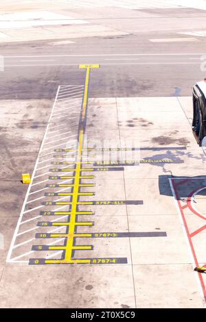 Vista ravvicinata ad angolo elevato delle marcature gialle dei cancelli aeroportuali sull'asfalto di fronte al cancello con strada di servizio e grembiule sullo sfondo Foto Stock