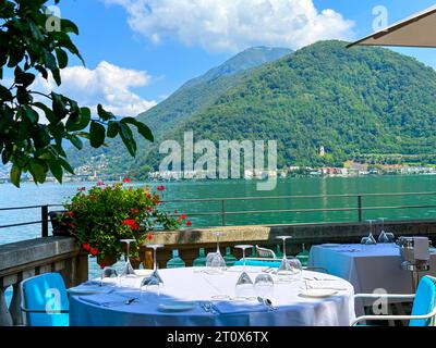 Vista panoramica sul Lago di Lugano con la montagna da un ristorante con tavolo in una soleggiata giornata estiva a Lugano, Ticino, Svizzera Foto Stock