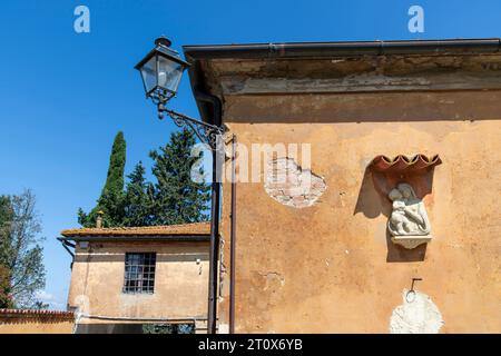 Vista dall'angolo basso della colorata facciata intonacata di case a Ghizzano, Italia conosciuta per le sue case colorate e le sculture con placca scultorea religiosa Foto Stock