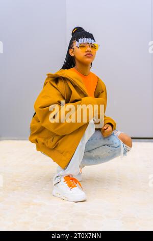 Una giovane ballerina con trecce. Black Ethnic Girl con T-shirt, occhiali da sole arancioni e Un Hunter, Urban pose Buck Foto Stock