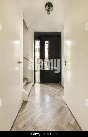 un ingresso con pavimento in legno e porta d'ingresso nera che conduce all'ingresso sulla sinistra è una parete bianca Foto Stock