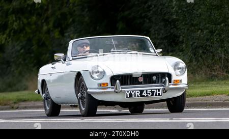 Bicester, Oxon., UK - 8 ottobre 2023: 1970 auto d'epoca bianca MGB che guida su una strada di campagna inglese. Foto Stock