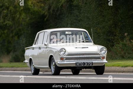 Bicester, Oxon., UK - 8 ottobre 2023: 1966 auto d'epoca Ford Cortina bianca che guida su una strada di campagna inglese. Foto Stock