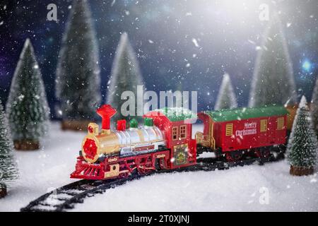 Trenino giocattolo sulla ferrovia nella neve con l'albero di Natale. Sfondo natalizio e Capodanno. Creativa composizione natalizia invernale. Foto Stock