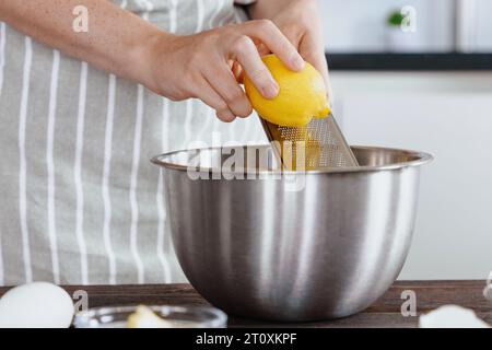 Le mani del cuoco grattugiano la scorza di limone in un recipiente di impasto. Sapore naturale in scorza di limone vidi. Preparare gli ingredienti in una panetteria o in un ristorante ki Foto Stock