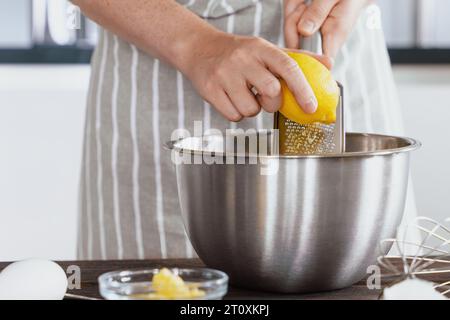 Le mani del cuoco grattugiano la scorza di limone in un recipiente di impasto. Sapore naturale in scorza di limone vidi. Preparare gli ingredienti in una panetteria o in un ristorante ki Foto Stock