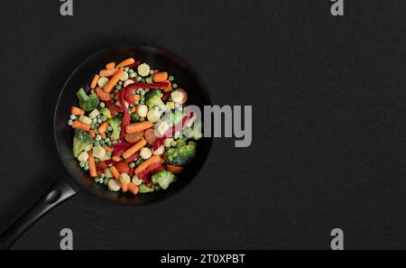 Padella per friggere con verdure surgelate a fette su sfondo nero. Insalata con mix di verdure. Vista dall'alto, base piatta. Copia spazio. Foto Stock