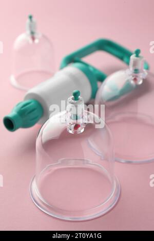 Coppe in plastica e tiralatte a mano su sfondo rosa, primo piano. Terapia di coppettazione Foto Stock