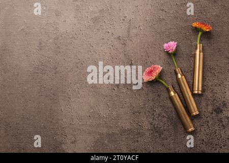 Bellissimi fiori in astucci di proiettile su un tavolo grigio testurizzato, piatto. Spazio per il testo Foto Stock