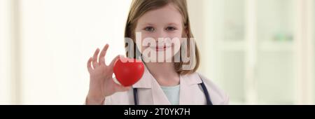 Bambina positiva in uniforme del medico tiene il cuore rosso Foto Stock