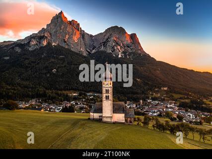 Seis am Schlern, Italia - Vista aerea di San Valentin e il famoso monte Sciliar sullo sfondo al tramonto con cielo dorato e blu e guerra Foto Stock