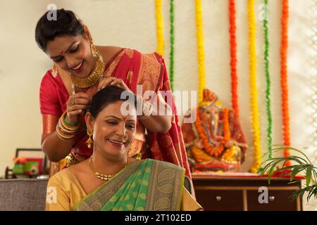 Nuora che aiuta la suocera mentre si prepara in occasione di Ganesh Chaturthi Foto Stock