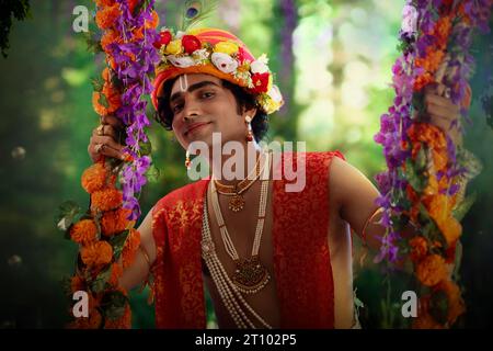 Giovane vestito da Lord Krishna e seduto su un altalena in occasione di Janmashtami Foto Stock