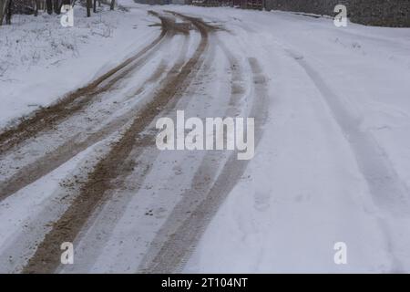 Piste per auto su una strada innevata. Strada sdrucciolevole, pericolo, rischio di slittamento. Tracce di battistrada per pneumatici invernali. Foto Stock