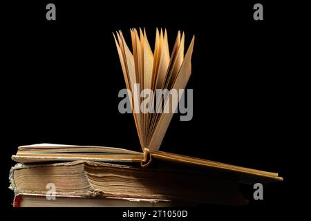 pila di vecchi libri con uno aperto in cima su sfondo scuro. Vecchi libri in biblioteca. Libreria. Pubblicazioni di conoscenza, letteratura. Libreria bo Foto Stock