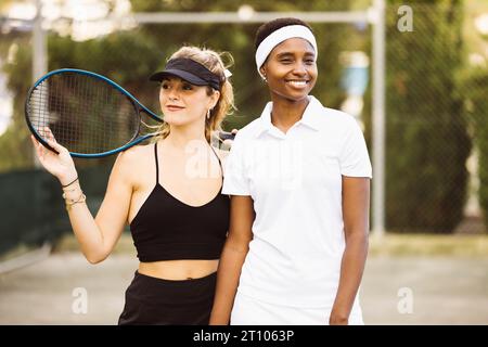 Ritratto di due giovani belle donne con vestiti da tennis e racchette in un campo da tennis pronto a giocare. Foto Stock