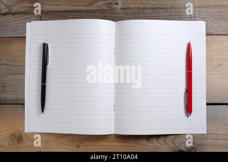 Quaderno scolastico aperto e due penne a sfera su sfondo in legno, vista dall'alto Foto Stock