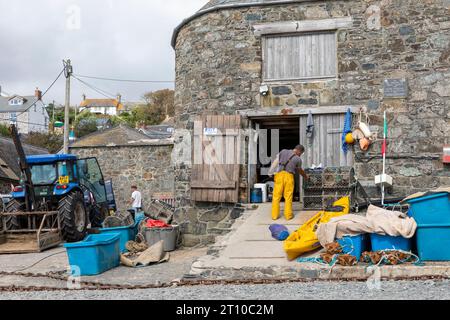 Cadgwith Cove pescatore in pelli di petrolio che lavora alla capanna da pesca, Cadgwith Village, Cornovaglia, Inghilterra, 2023 Foto Stock