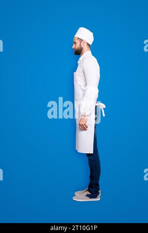 Profilo vista laterale snap, corpo ritratto a grandezza naturale di bella macellaio attraente isolato su sfondo grigio, indossando camicia bianca, grembiule, jeans Foto Stock