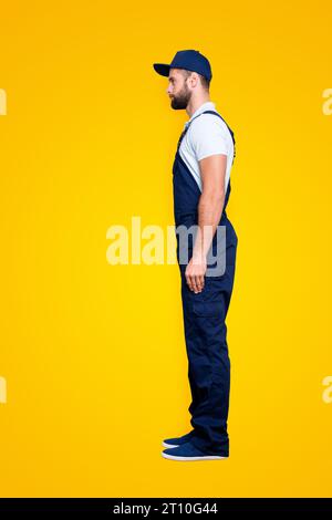 Profilo del corpo full-size verticale, scatto di attraente, sicuro offrire in blu uniforme con barba corta, isolato su sfondo grigio Foto Stock