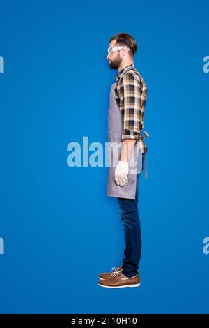 Bottoncino per il corpo di dimensioni normali, vista laterale metà faccia ritratto di carpentiere seducente e calmo con acconciatura in occhiali di sicurezza, jeans, sfondo grigio isolato Foto Stock