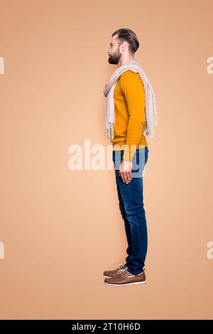 Full size fullbody snap, vista laterale metà faccia ritratto di bel stilista attraente in maglione, jeans con sciarpa intorno al collo isolato sul grigio Foto Stock