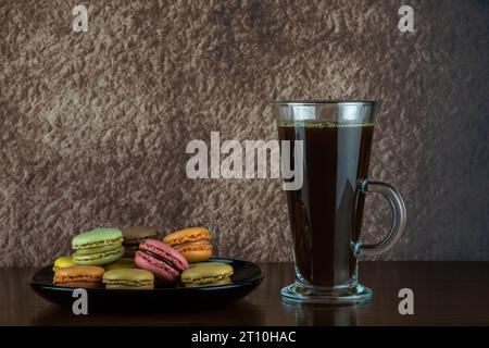 Pila di biscotti macaron e bicchiere di caffè nero su una superficie di legno Foto Stock