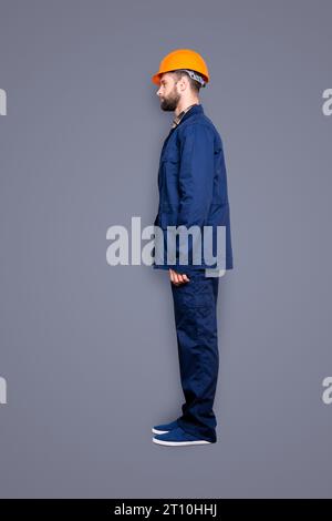 Bottoncino full-body con gambe, profilo ritratto di un bel riparatore calmo in uniforme blu, isolato su sfondo grigio Foto Stock