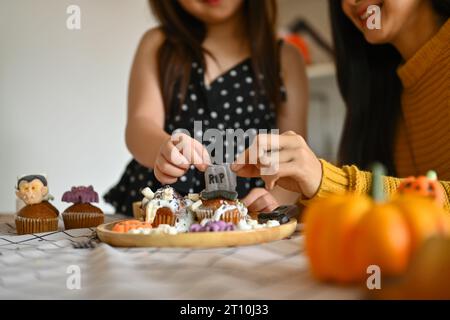 Foto corta di bambina che decora i cupcake di Halloween con mostri, zucche e fantasmi diversi Foto Stock