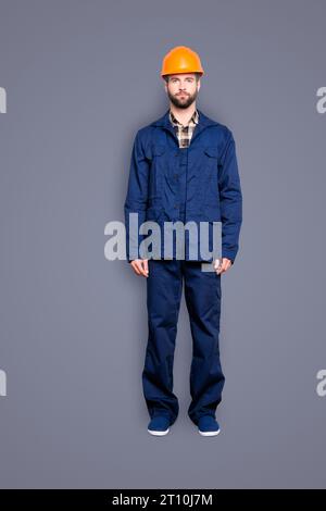 Ritratto integrale con gambe di un bel riparatore virile in uniforme blu, isolato su sfondo grigio, guardando la telecamera Foto Stock