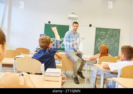 Vista posteriore del ragazzo che solleva la mano durante la lezione in classe a scuola Foto Stock