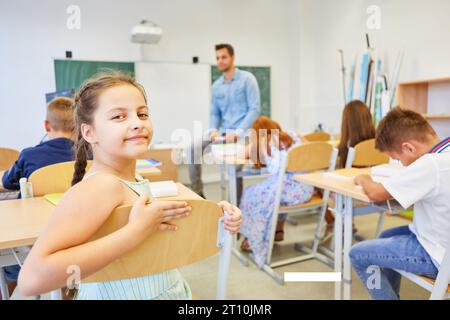 Ritratto di una studentessa sorridente seduta sulla sedia con gli amici in classe Foto Stock