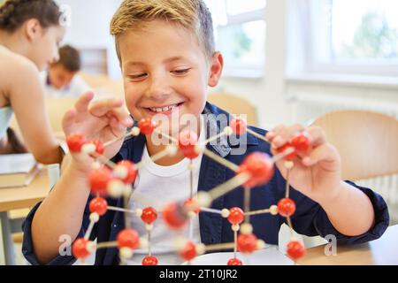 Studente felice che tocca la struttura molecolare mentre è seduto in classe Foto Stock