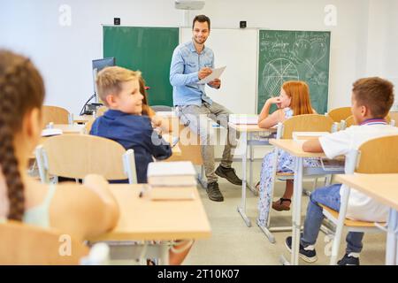 Felici studenti maschi e femmine seduti con l'insegnante in classe a scuola Foto Stock