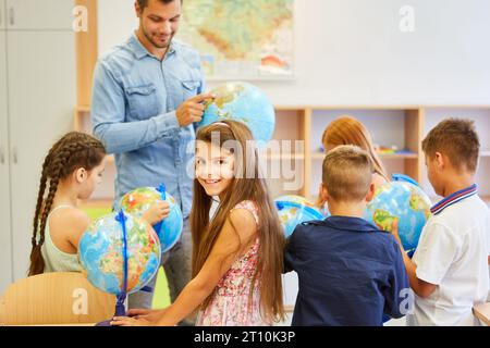 Ritratto di una studentessa con studenti che usano globi in classe di geografia Foto Stock