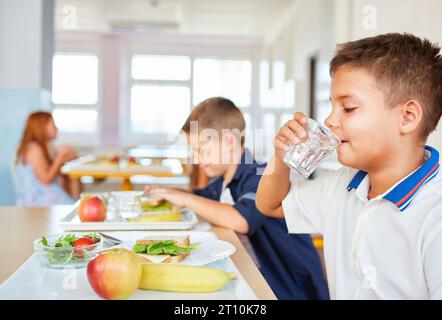 Scolaro che beve acqua dal bicchiere mentre pranza nella caffetteria Foto Stock