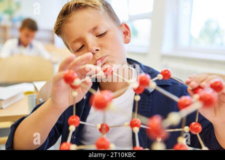 Curioso studente elementare maschile che esamina la struttura molecolare in classe Foto Stock