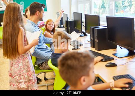Studenti elementari maschili e femminili che discutono con l'insegnante in classe informatica a scuola Foto Stock