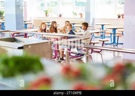 Sorridenti studenti maschili e femminili che pranzano seduti a tavola durante il pranzo nella mensa scolastica Foto Stock