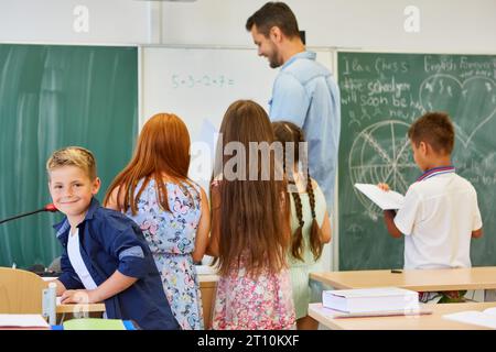 Sorridente ragazzo con amici che fa matematica con insegnante in classe Foto Stock