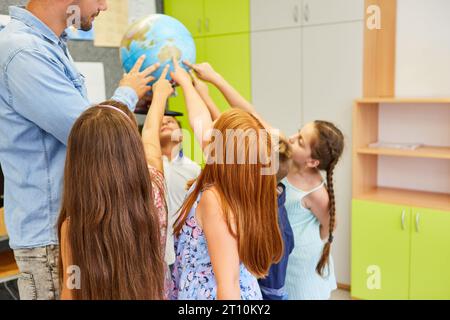 Studenti elementari che puntano al globo tenuti da insegnanti in classe di geografia Foto Stock