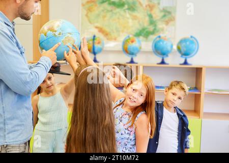 Insegnante maschile che tiene globo tra studenti elementari in classe di geografia Foto Stock