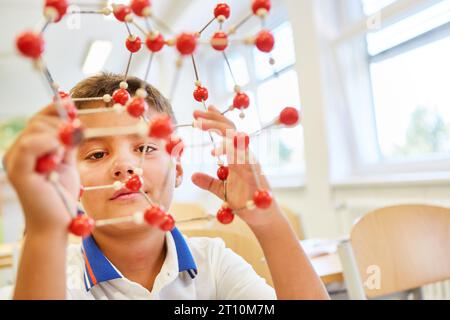 Scolaro con struttura molecolare seduto in classe alla scuola elementare Foto Stock