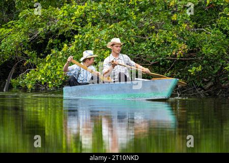 Due giovani uomini mennoniti che pescano da una piccola barca fatta in casa sul New River nel quartiere Orange Walk del Belize. Foto Stock