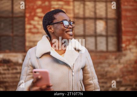Ritratto all'aperto di felice donna afro-americana. Sta utilizzando lo smartphone. Foto Stock