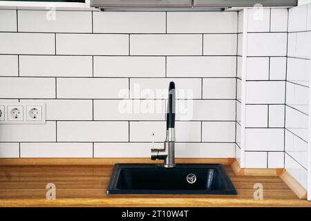 Elegante lavello nero e rubinetto su un piano di legno in una cucina da vicino Foto Stock