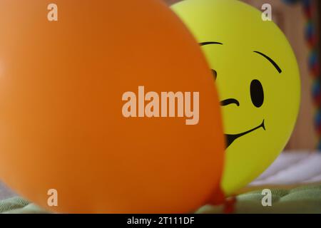 Palloncini gialli e arancioni. Due palloncini ad aria calda appoggiati sul tappeto. Palloncino giallo con faccia sorridente. Decorazioni per feste di compleanno Foto Stock