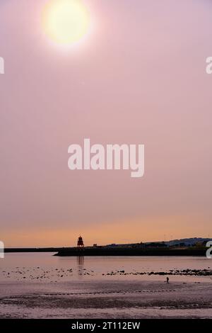 Luce del sole autunnale sull'estuario del Tyne e sul faro d'epoca di Herd Sands con un pescatore che cerca la ragma Foto Stock