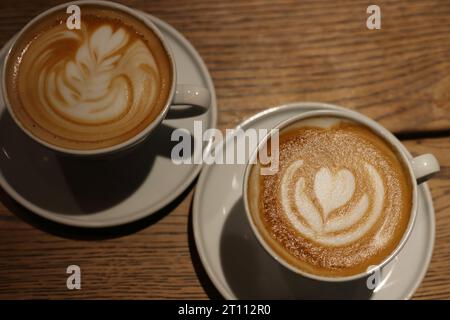 Due tazze di cappuccino gourmet della caffetteria sul tavolo di legno. Latte da caffè con schiuma cremosa sulla parte superiore. Sfondo di legno. Caffe' latte art nella caffetteria. In alto Foto Stock